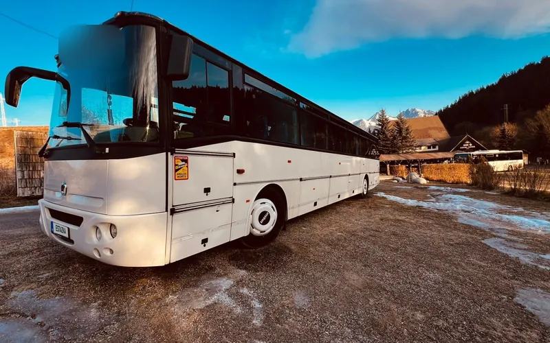 Biely linkový autobus na parkovisku pod horami
